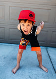 Child wearing a red Jurassic Snapback and colorful outfit standing on a blue surface with a gray garage door background