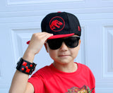 Child wearing a black and red Jurassic Snapback with a dinosaur logo, sunglasses, and a matching wristband against a light blue wall.
