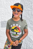 Child wearing a 'Jurassic Park' themed t-shirt and Jurassic Snapback against a textured white wall.