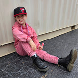 Child in pink outfit sitting on pavement next to a white container