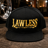 A black flat-brim baseball cap with 'LAWLESS' embroidered in ornate gold lettering across the front, photographed on a dark textured surface with a blurred car wheel and warm interior lights in the background.