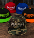 Five flat-brim snapback caps arranged on a wooden surface, each with the text 'DEGENERATE SOCIAL CLUB' embroidered on the front. The front cap is camouflage in green, brown, and tan, while the rear caps are red, blue, black with neon green, and black with orange brims.